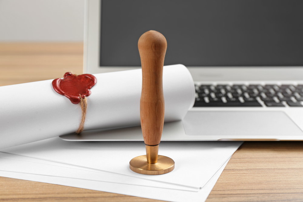 Notary's public pen and sealed document near laptop on wooden table, closeup