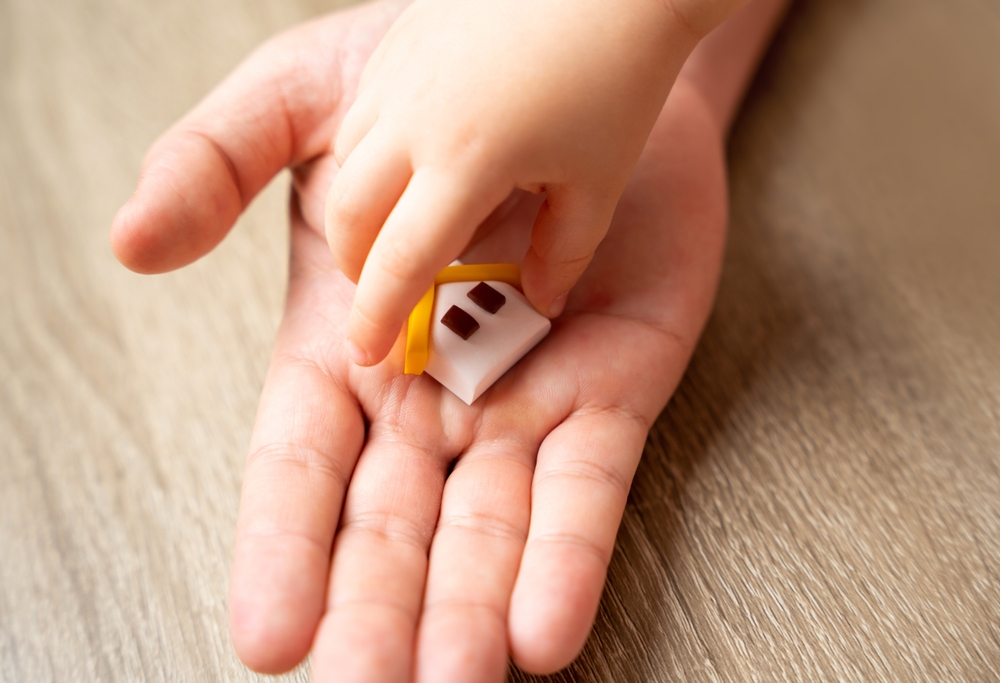 A child's hand takes a house from an adult's hand. The concept of transfer of property and inheritance. Real estate. housing as a gift, apartment or house
