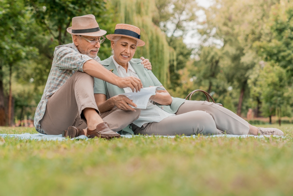 Happy Mature couple reading the book together and having picnic in the garden at the summer day. Retirement, Picnic, Relax, Older, Lover and dating concept.